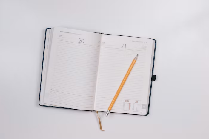 Buku agenda terbuka dengan lembaran kosong dan pensil di sampingnya untuk kebutuhan kerja harian.