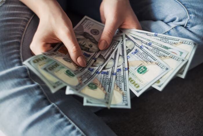 Tangan memegang beberapa lembar uang dolar AS, menunjukkan konsep keuangan atau pembayaran.