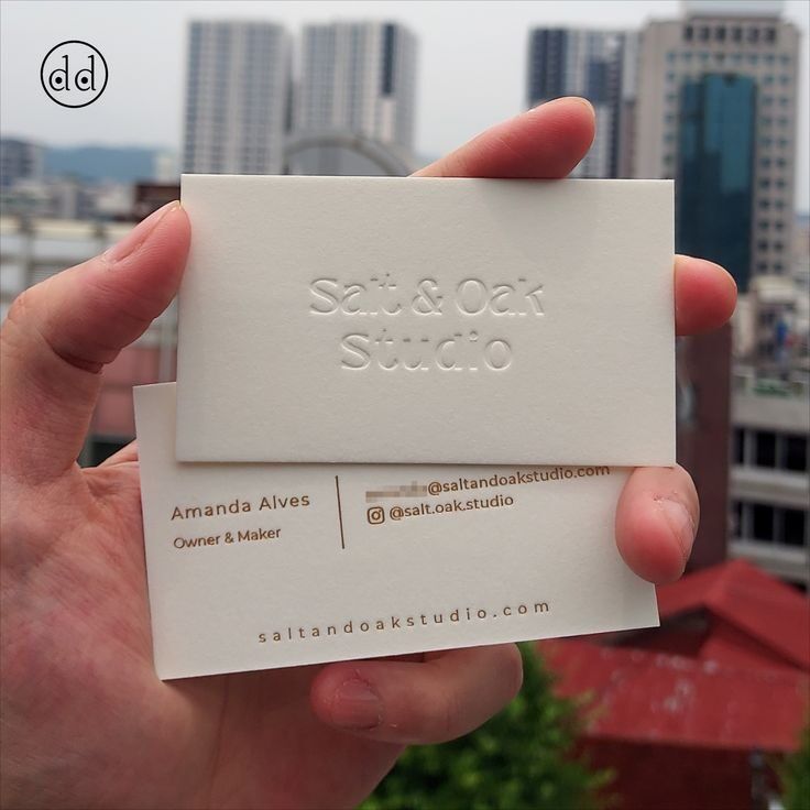 Tangan memegang kartu nama putih dengan logo dan detail kontak 'Salt & Oak Studio'.