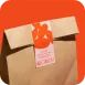 Kotak hadiah karton oranye dengan tag putih dan pita kecil.