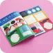 Beberapa brosur glossy berisi halaman berwarna tersusun di atas latar merah muda.